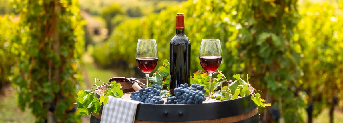 a bottle of red wine and two wine glasses are located ontop of a barrel