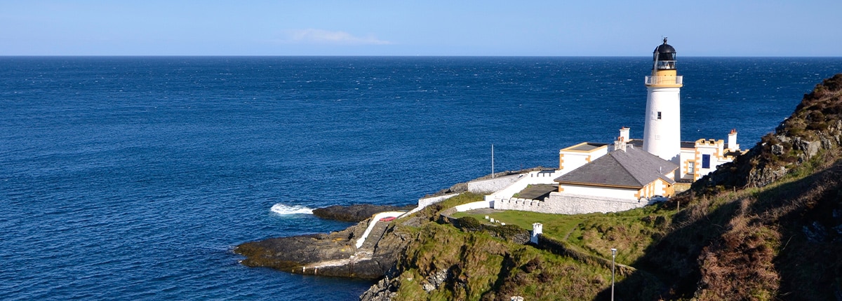 a white lighthouse is located a hillside