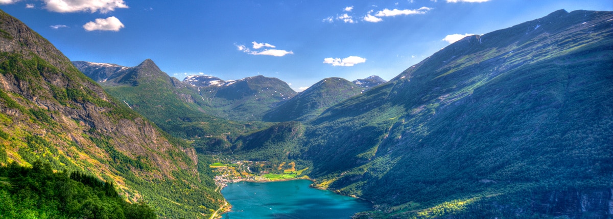 colorful mountains full of plant life surrounds a blue fjord