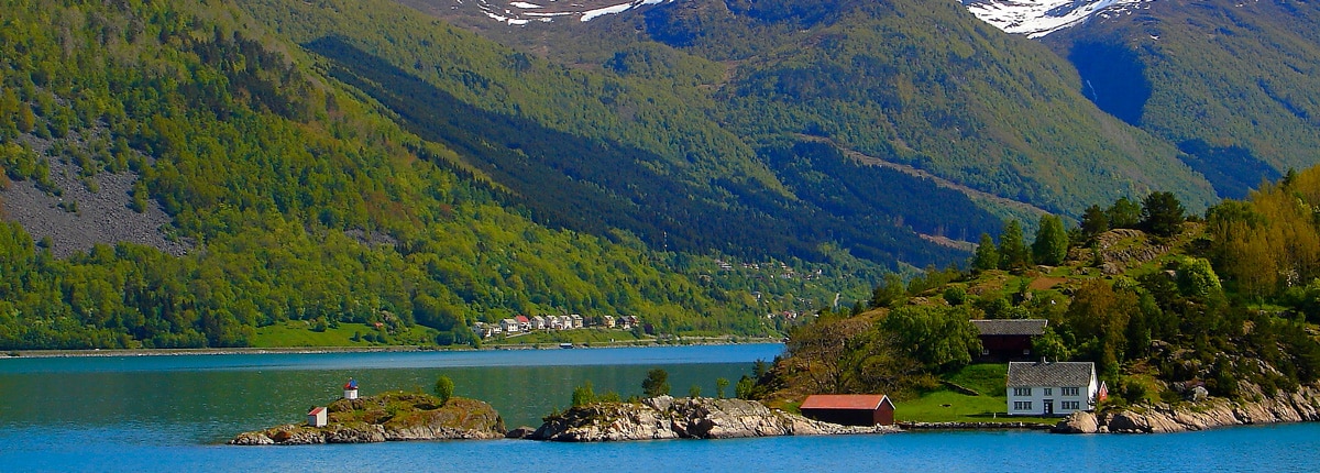 a small house sits on an inlet surrounded by water and green mountains