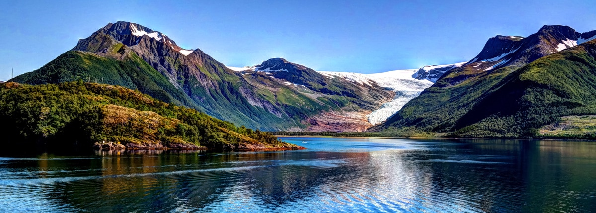 fjord surrounded by snowcapped mountains with lush green bases