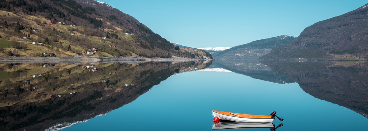 a small motor boat floats on the still blue waters of a fjord surrounded by mountains