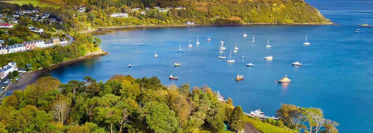 view of the green mountains and blue waters of portree, isle of skye, scotland