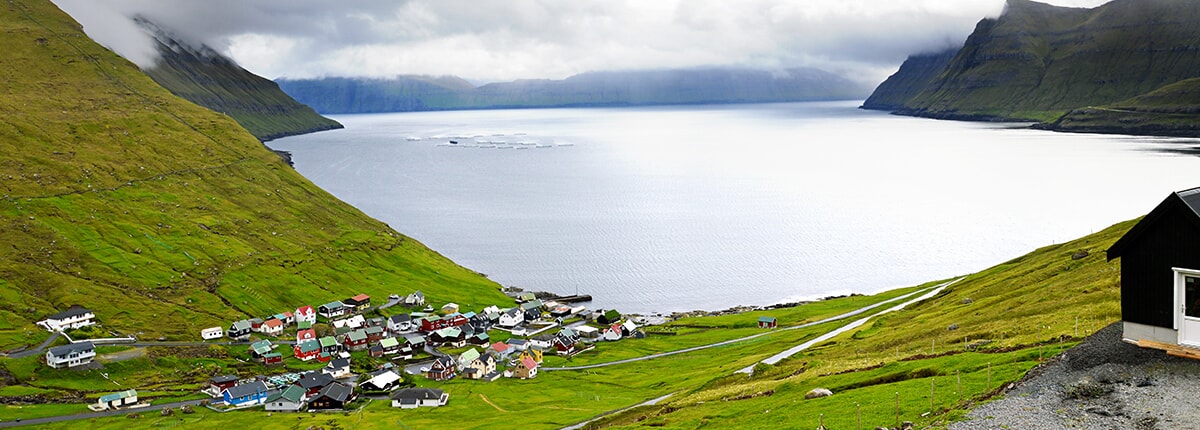 a green valley with view of the houses nestled along the water in runavik, faroe islands