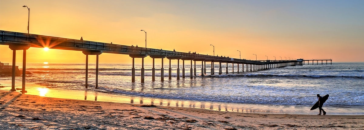 san diego sunset on the beach with surfer holding a surfboard