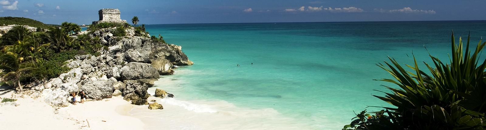 Small quaint beach with crystal blue waters alongside palm trees and rocks