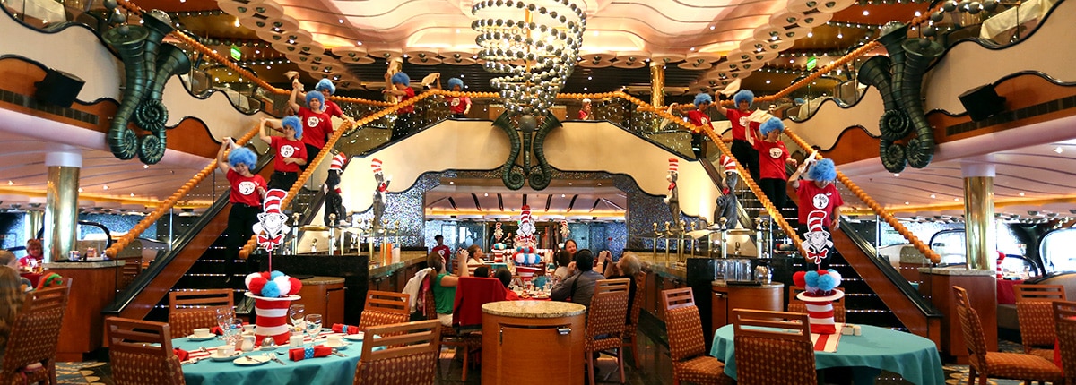 dining room setting with carnival staff walking down the stairs wearing wigs