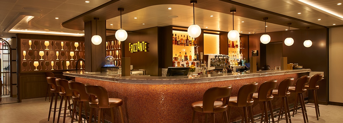 a background wall of different wine glasses and brown chairs at the counter of the frizzante bar