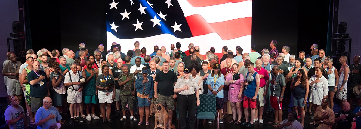 military guests with hands over hearts during national anthem with the American flag in the background